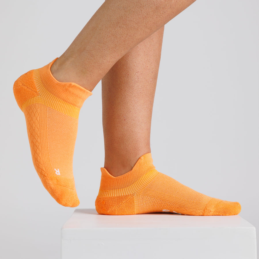 Orange ankle grip socks worn on a display block, showing side and top views. By Squid Socks.