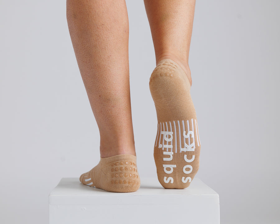 Tan no-show grip socks worn on a display block, with one sole raised to show white bottom grips. By Squid Socks.
