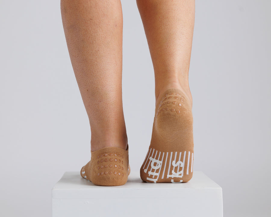 Brown no-show grip socks viewed from behind, with one sole raised to show bottom grips. By Squid Socks.