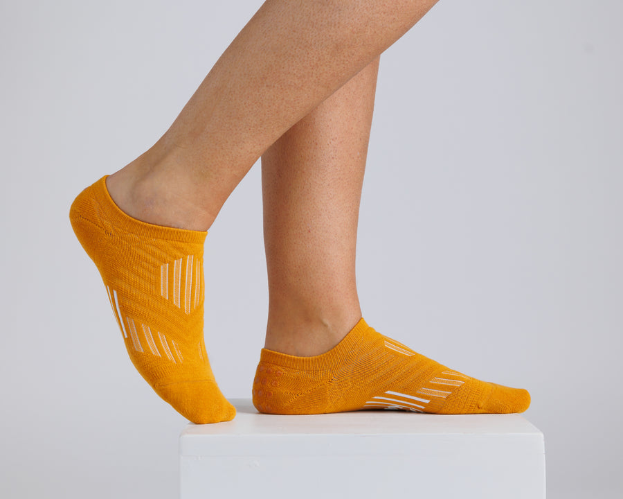 Mustard yellow no-show grip socks worn on a display block, showing side and top views. By Squid Socks.