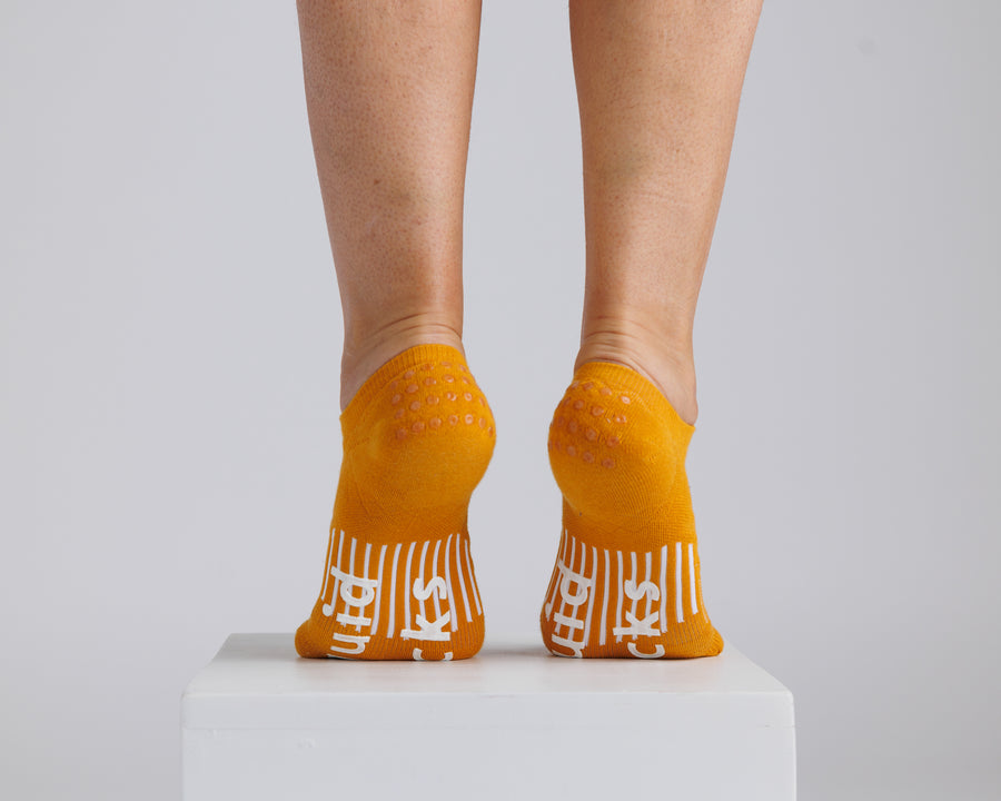 Mustard yellow no-show grip socks viewed from behind, showing heel and bottom grips. By Squid Socks.