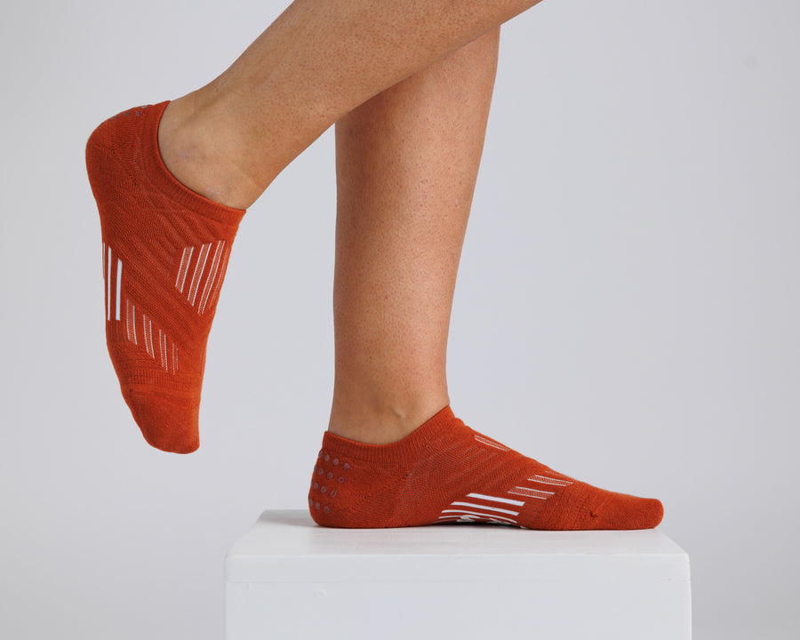 Rust orange no-show grip socks worn on a display block, showing side and top views. By Squid Socks.