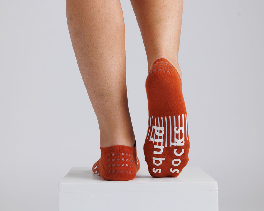 Rust orange no-show grip socks with one sole raised to show white bottom grips. By Squid Socks.