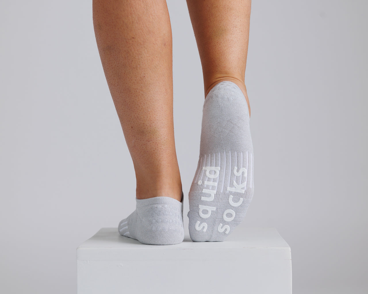 Gray no-show grip socks with one sole raised to show white bottom grips. By Squid Socks.