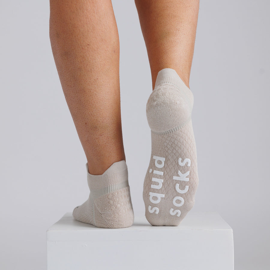 Cream ankle grip socks viewed from behind, with one sole raised to show white bottom grips. By Squid Socks.