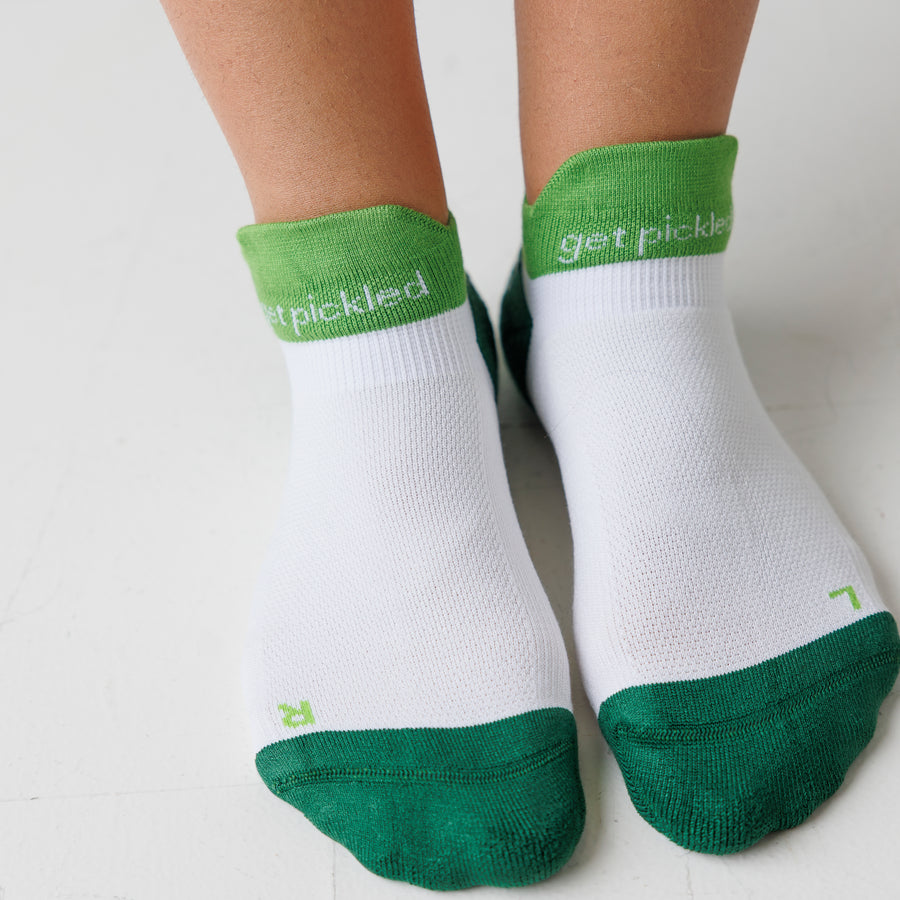 White and green ankle pickleball grip socks worn on both feet, with 'get pickled' lettering around the cuffs. By Squid Socks.