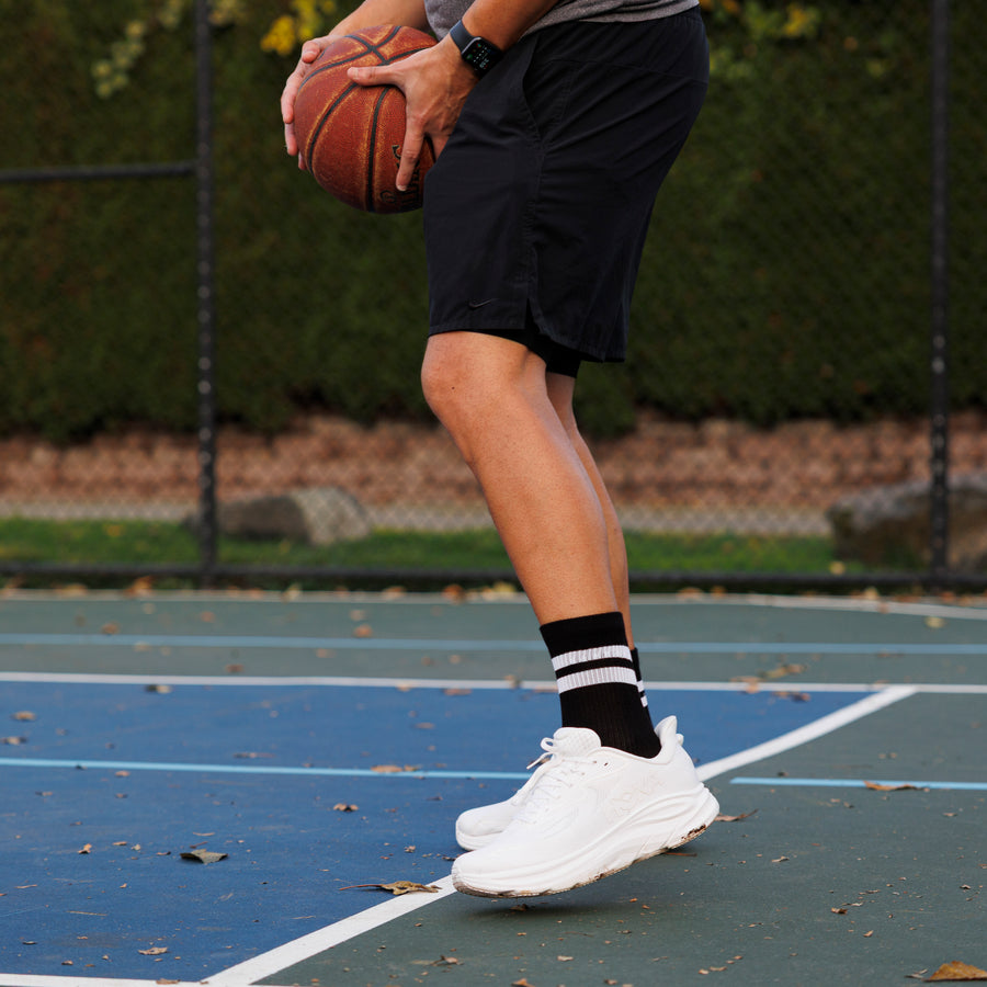 Person wearing black striped crew grip socks and white sneakers while holding a basketball on a court. By Squid Socks.