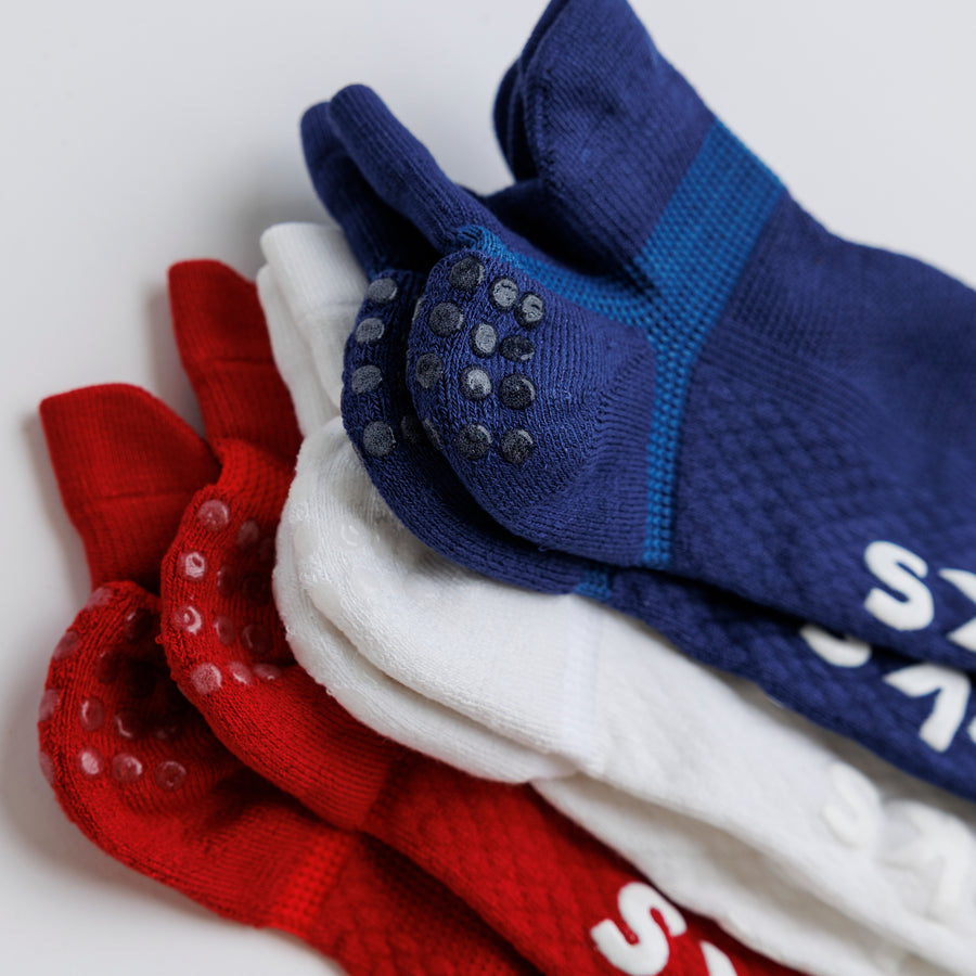 Close-up of stacked navy, white, and red ankle socks with heel grip dots visible. By Squid Socks.