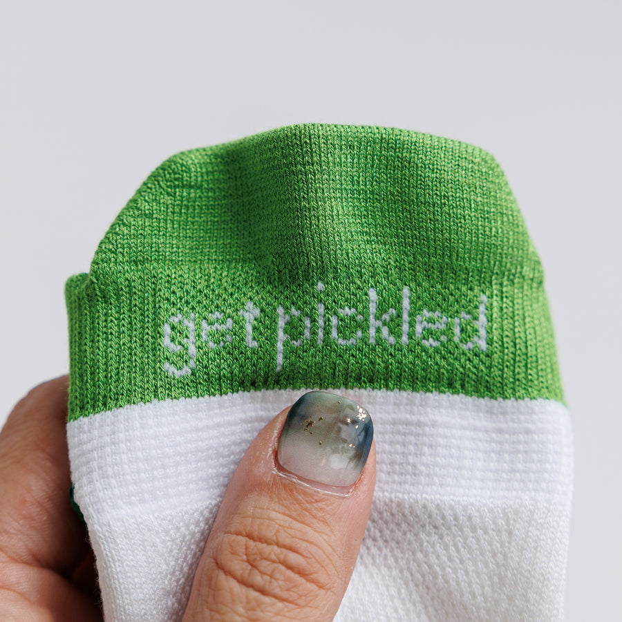 Hand holding a white and green ankle pickleball sock cuff with 'get pickled' lettering. By Squid Socks.