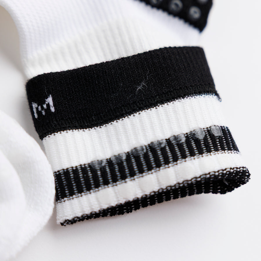 Close-up of a white and black striped crew sock cuff, with the medium size marking visible. By Squid Socks.