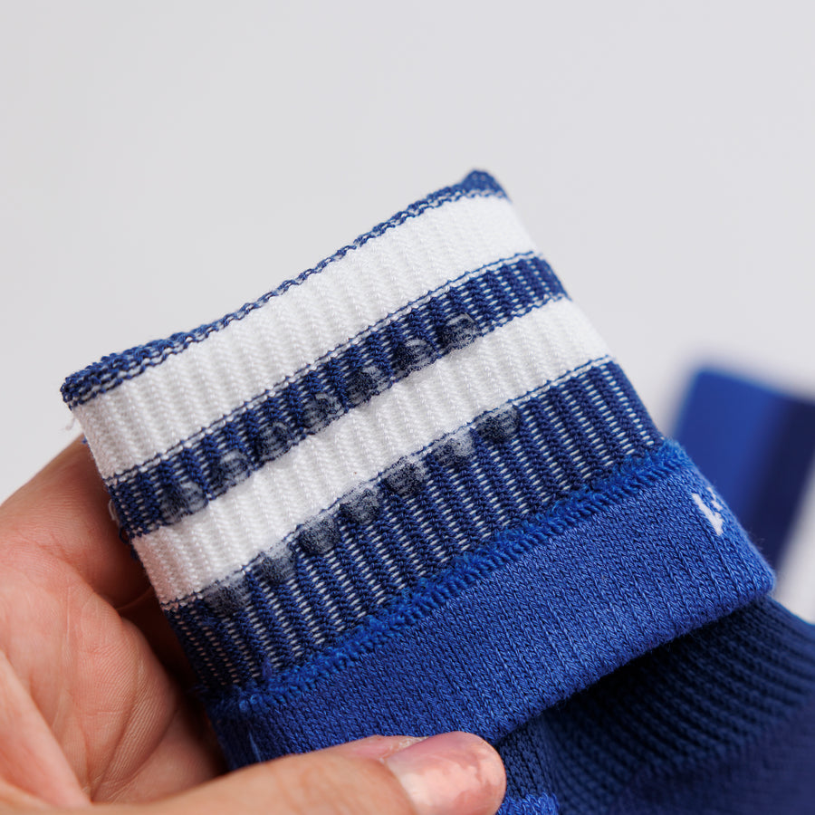 Hand holding a navy striped crew sock cuff folded back to show the interior grip dots. By Squid Socks.