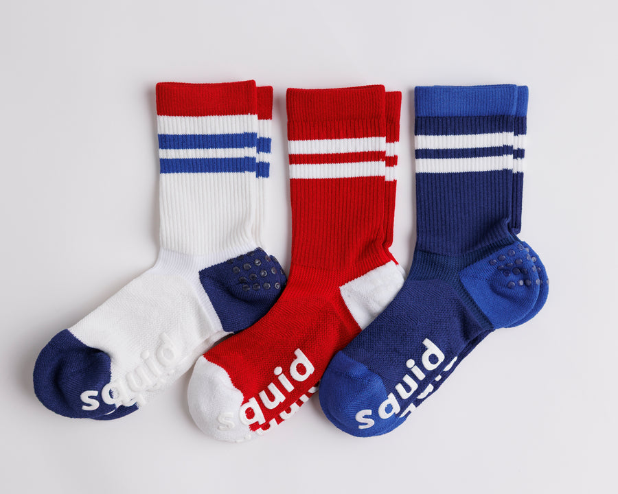 All-American crew grip socks in white, red, and navy, arranged flat with striped cuffs visible. By Squid Socks.