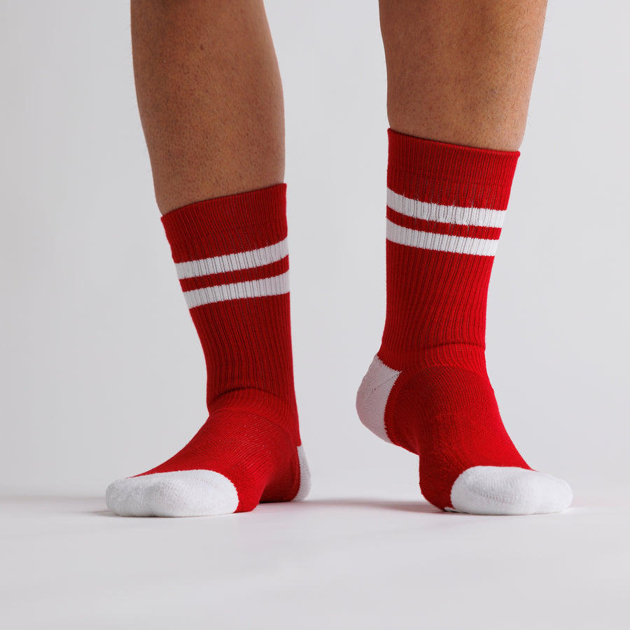 Red All-American crew grip socks with white stripes and toe panels worn on both feet. By Squid Socks.