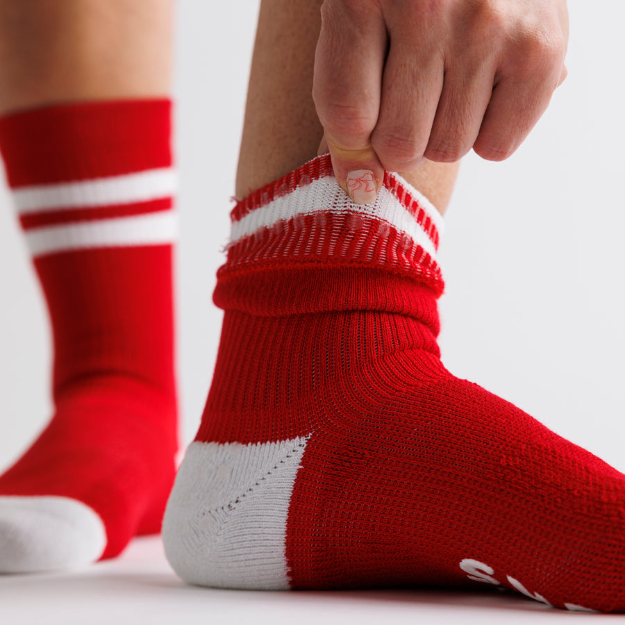 Person pulling back the cuff of a red crew grip sock with white stripes. By Squid Socks.