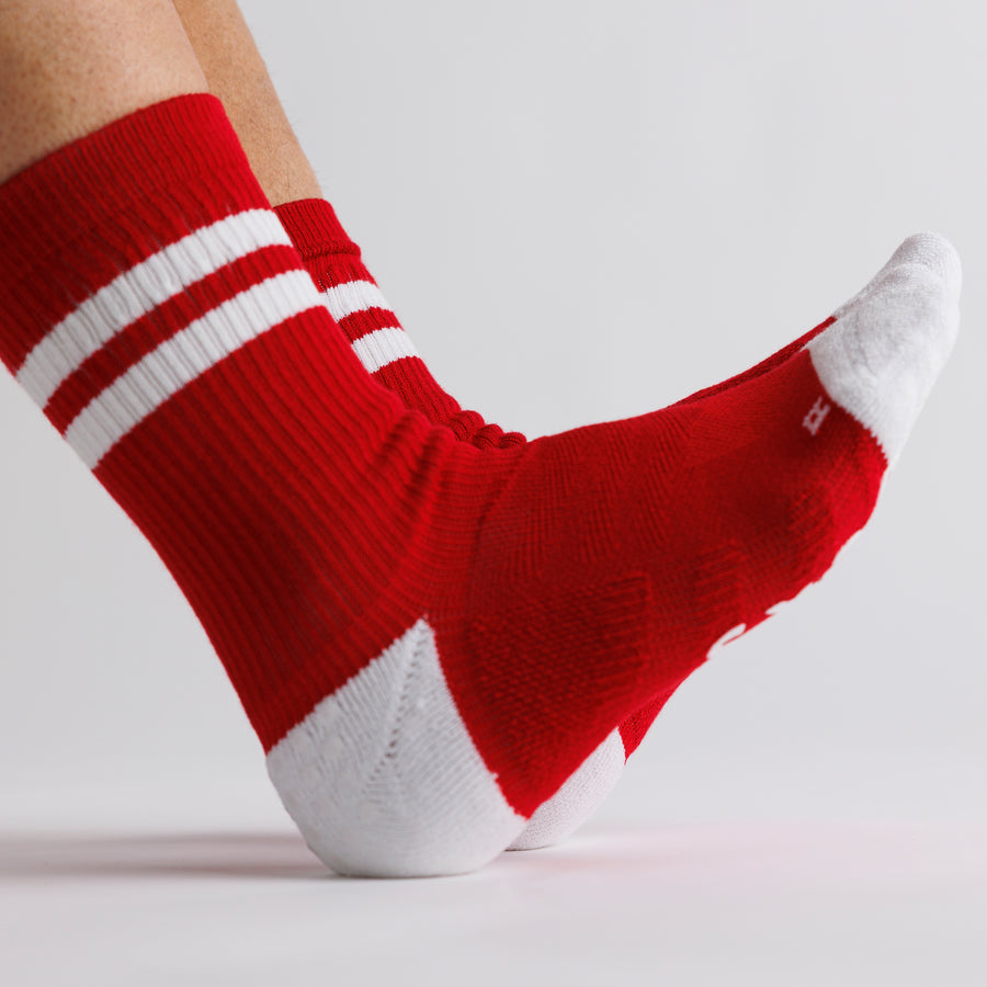 Side view of a red crew grip sock with white stripes, toe, and heel, with toes raised. By Squid Socks.