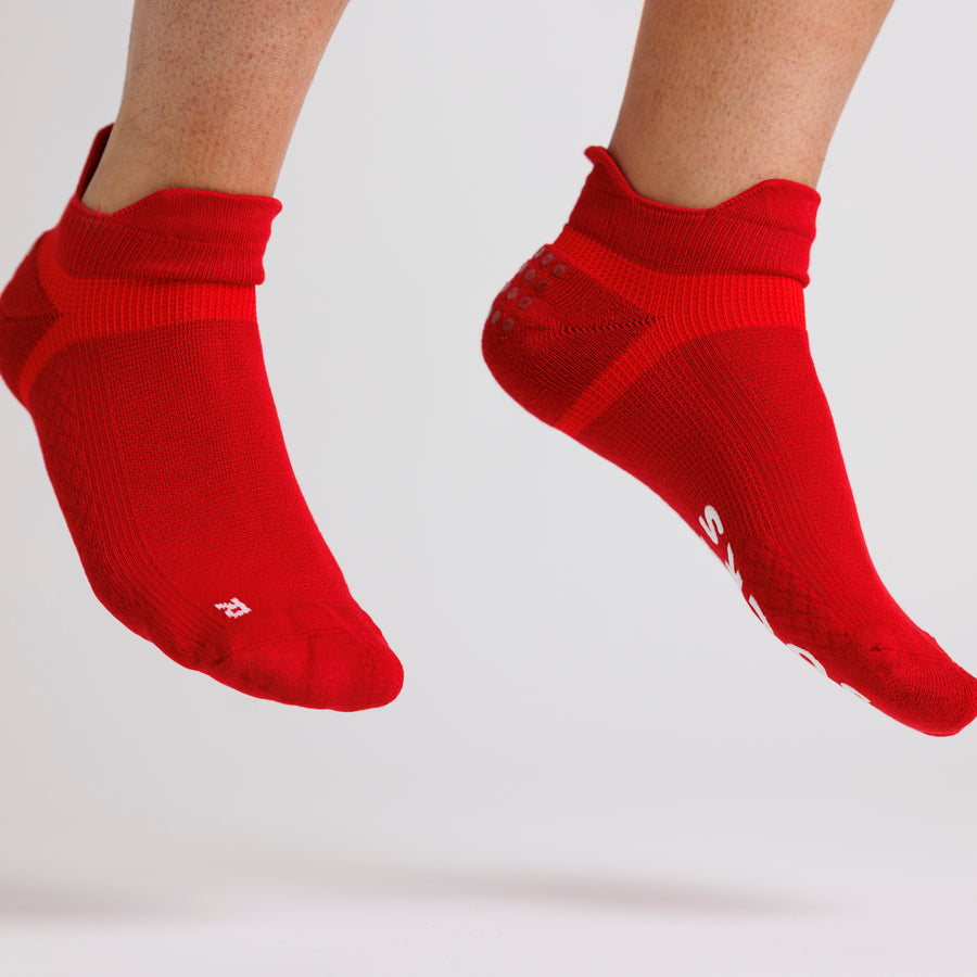 Red ankle grip socks worn on both feet, lifted above the floor. By Squid Socks.