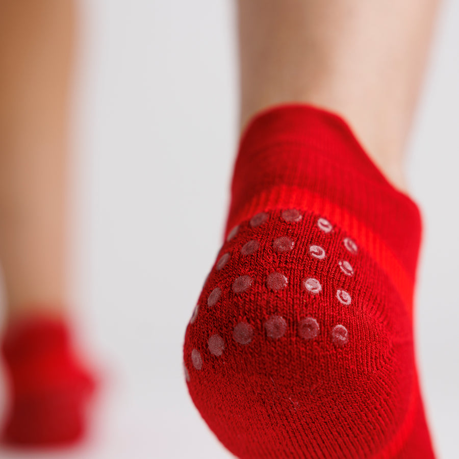 Close-up of a red ankle sock worn on the foot, showing grip dots on the heel. By Squid Socks.