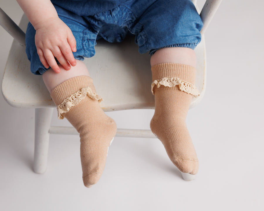 Candace kids socks: child seated on a chair wearing beige lace-trim socks. Squid Socks, the brand seen on Shark Tank.