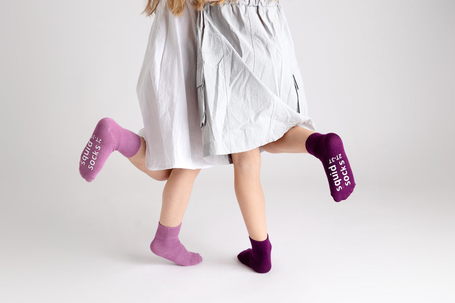 Orchid kids socks: children wearing lavender and plum socks while standing. Squid Socks, the brand seen on Shark Tank.