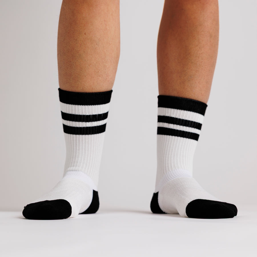 White Retro crew grip socks with black stripes, toe panels, and heels, worn on both feet. By Squid Socks.
