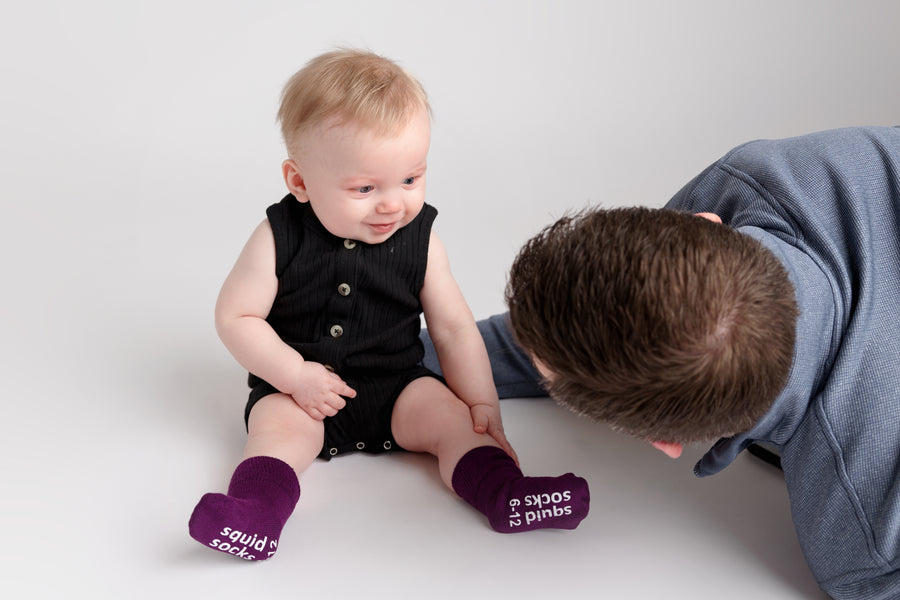 Orchid kids socks: adult playing beside a baby wearing plum socks. Squid Socks, the brand seen on Shark Tank.