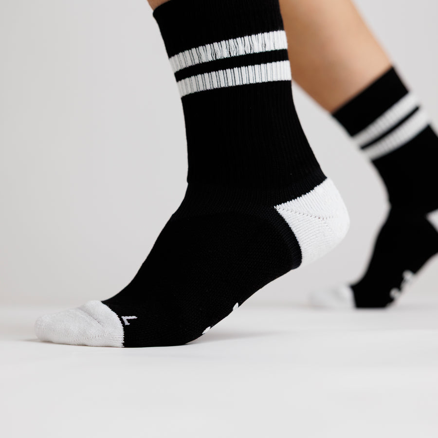 Black Retro crew grip socks with white stripes and toe panels, worn with one heel raised. By Squid Socks.