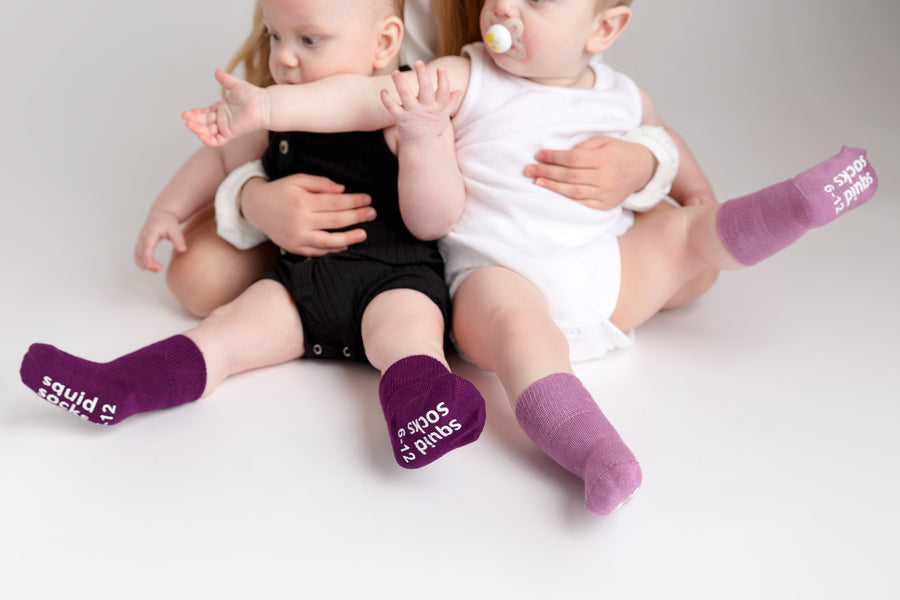 Orchid kids socks: two babies seated in plum and bright lavender socks. Squid Socks, the brand seen on Shark Tank.