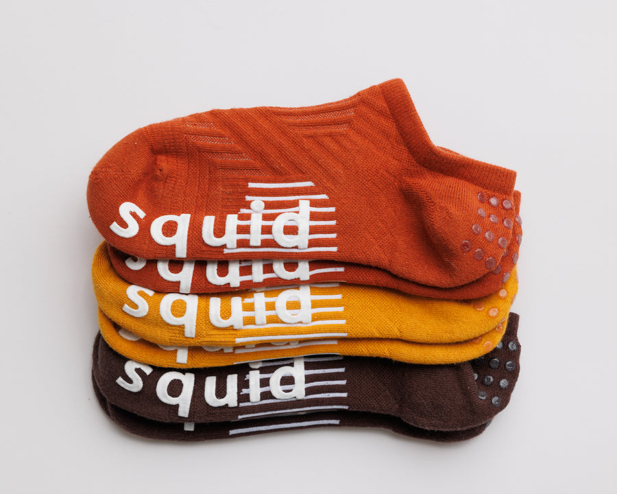 Fall Fanatic no-show grip socks in rust orange, mustard yellow, and brown, stacked to show all three colors. By Squid Socks.