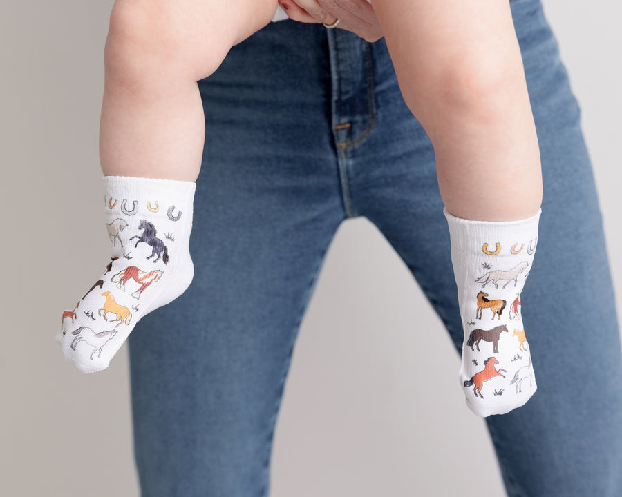 Cowboy kids socks: adult holding a baby wearing horse-print socks. Squid Socks, the brand seen on Shark Tank.