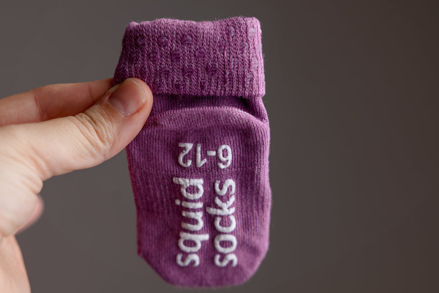 Orchid kids socks: hand holding a bright lavender sock showing sole grips. Squid Socks, the brand seen on Shark Tank.