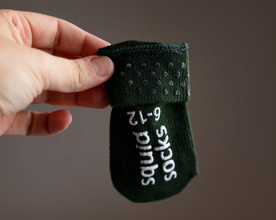 Cypress kids socks: hand holding a dark green sock showing cuff and sole grips. Squid Socks, the brand seen on Shark Tank.