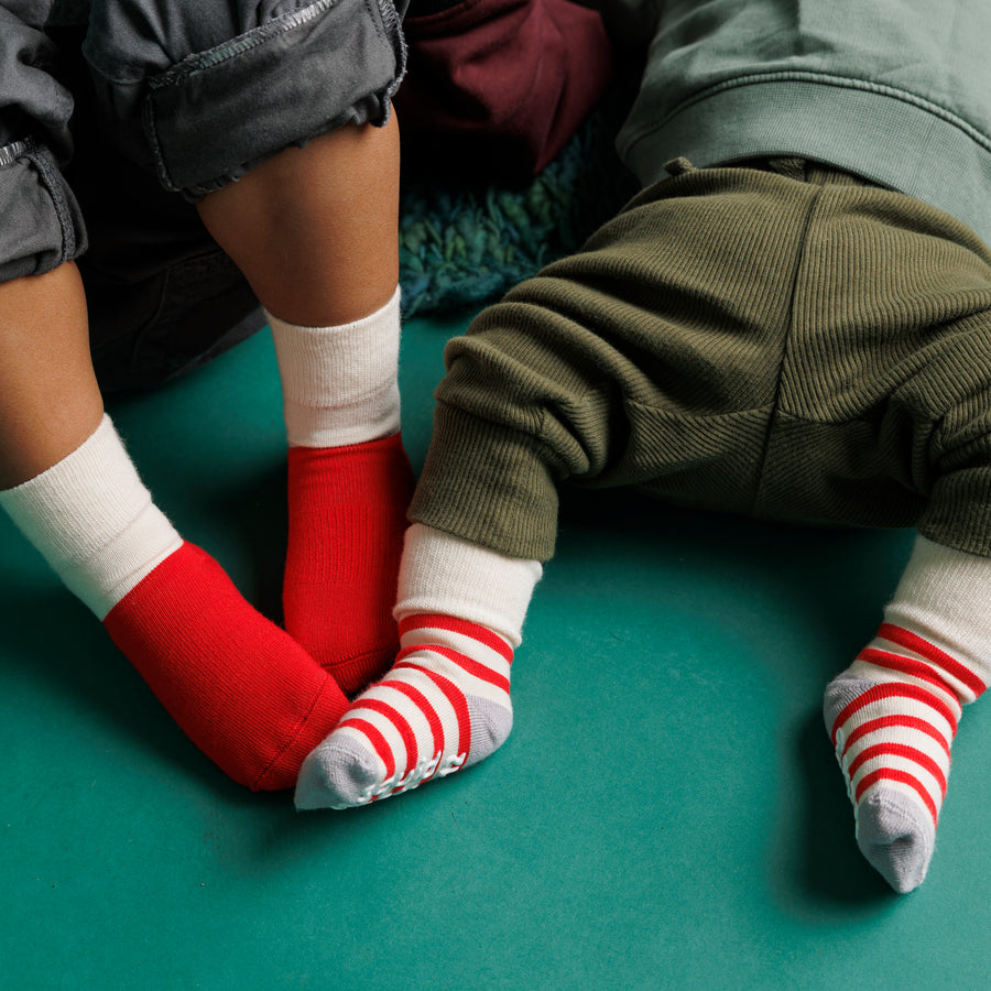 Adult seated beside a baby wearing Caroler Christmas grip socks.