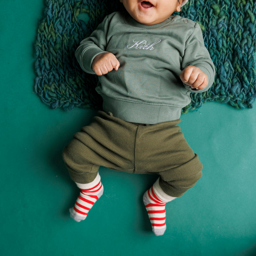 Baby lying on a green blanket wearing red and cream striped Caroler grip socks.