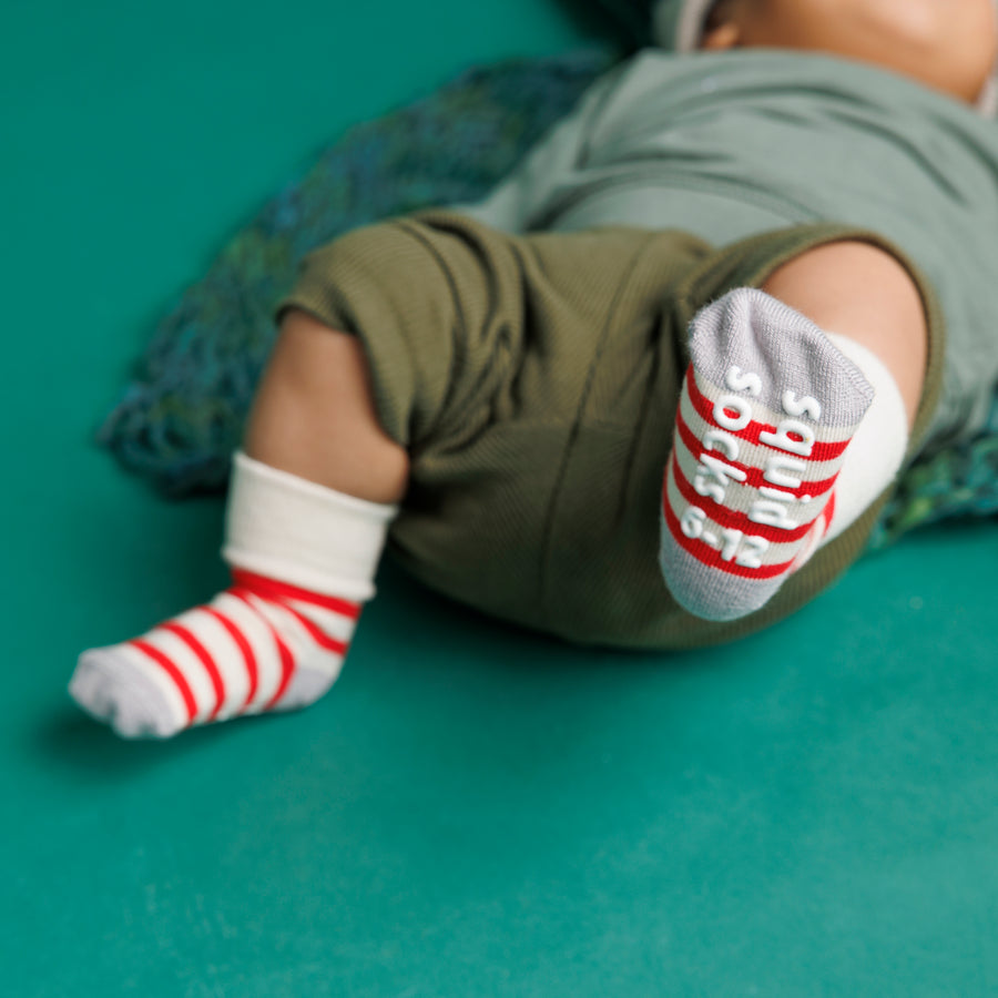 Baby wearing red and cream striped Caroler grip socks with one sole facing forward.