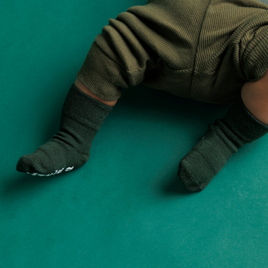 Baby wearing dark green Caroler grip socks on a green blanket.