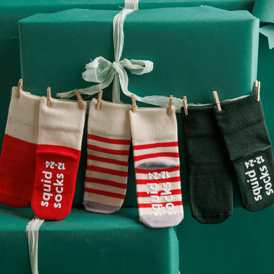 Caroler Christmas grip socks displayed beside green gift boxes.