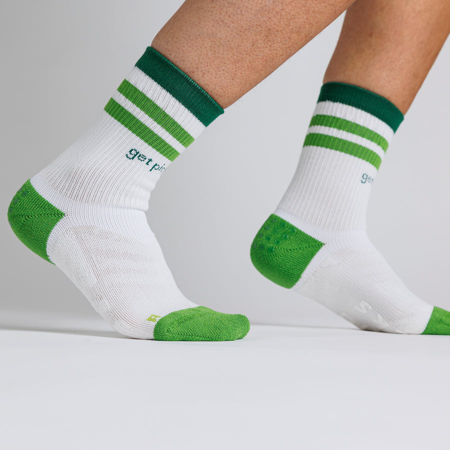White and green Pickle Pack crew pickleball grip socks worn with one heel raised. By Squid Socks.