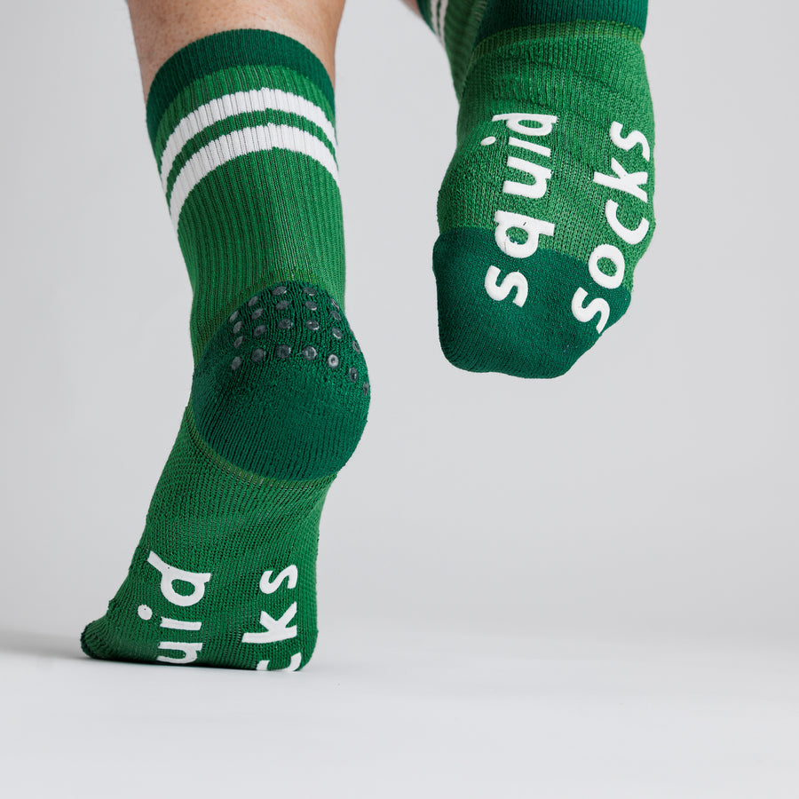 Green striped crew pickleball grip socks viewed from behind, with one sole raised to show white bottom grips. By Squid Socks.