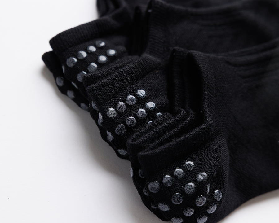 Close-up of stacked black no-show socks showing rows of grip dots on the heels. By Squid Socks.