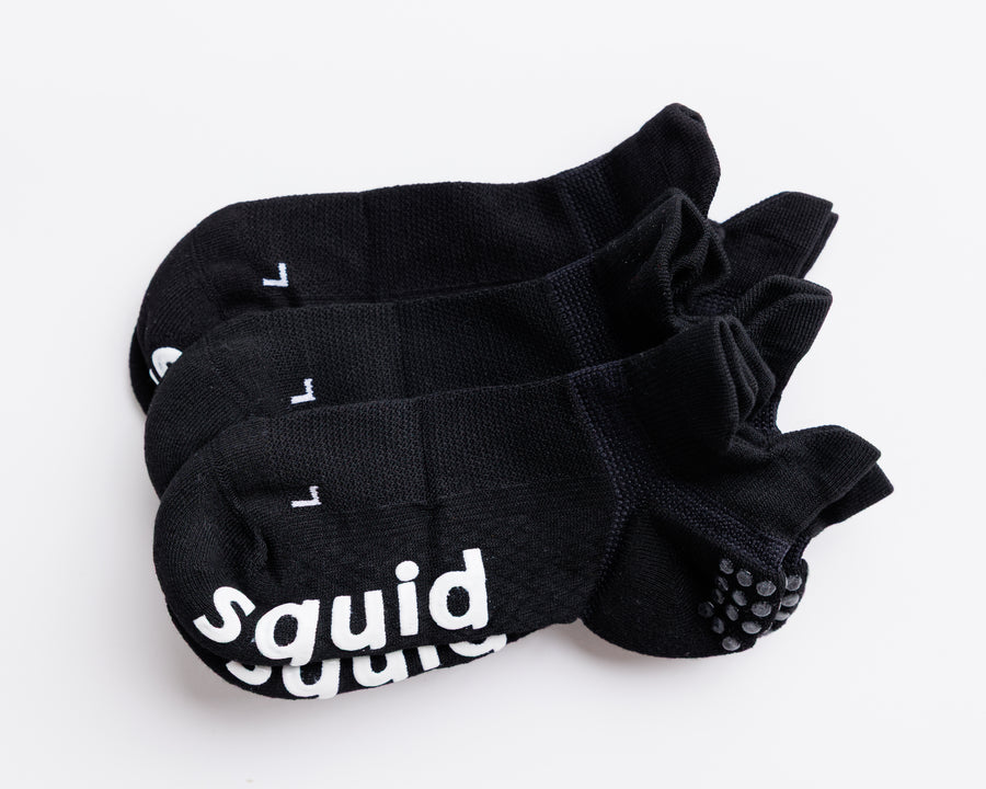 Blackout ankle grip socks arranged together, showing heel tabs and white bottom grips. By Squid Socks.