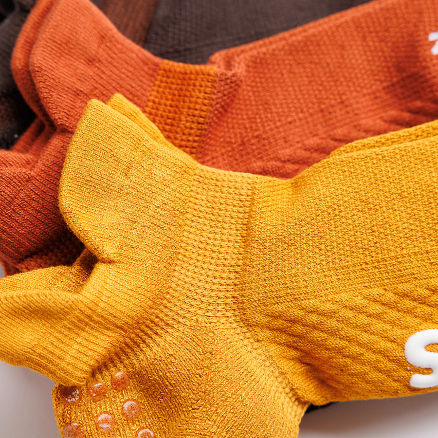 Close-up of mustard yellow and rust orange ankle socks showing heel tabs and grip dots. By Squid Socks.