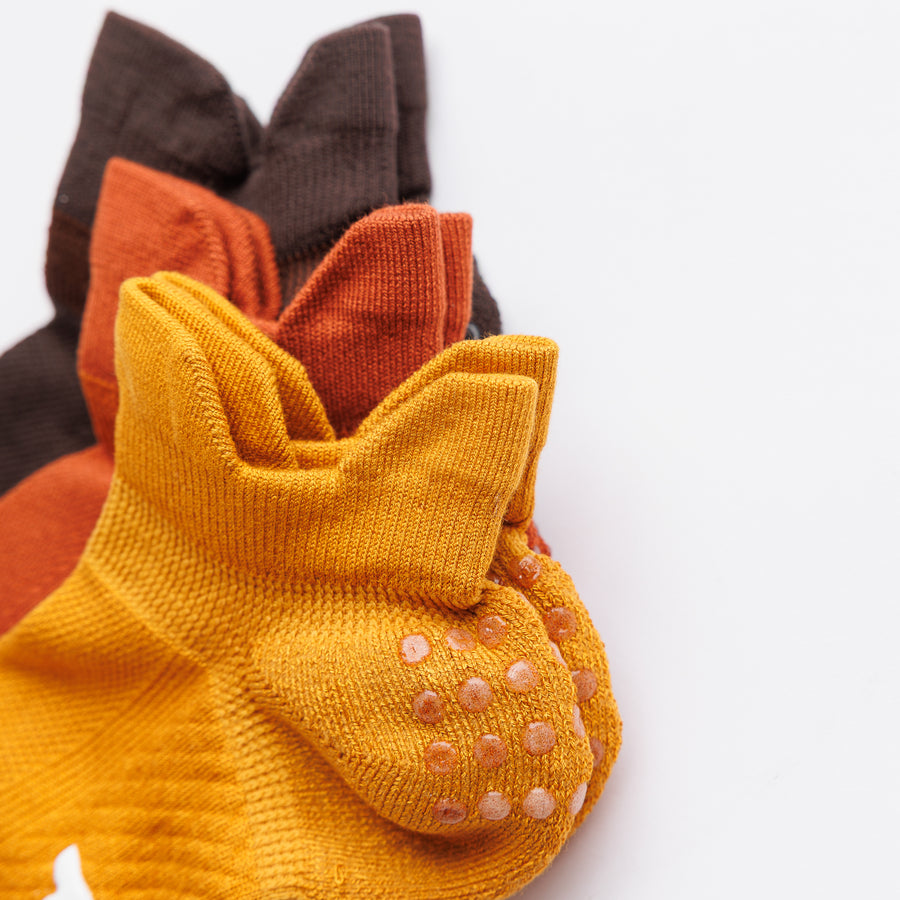 Close-up of stacked Fall Fanatic ankle socks showing grip dots on the mustard yellow heel. By Squid Socks.