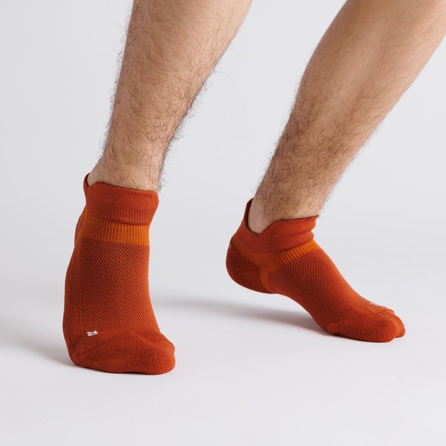 Rust orange ankle grip socks worn on both feet with one foot lifted. By Squid Socks.