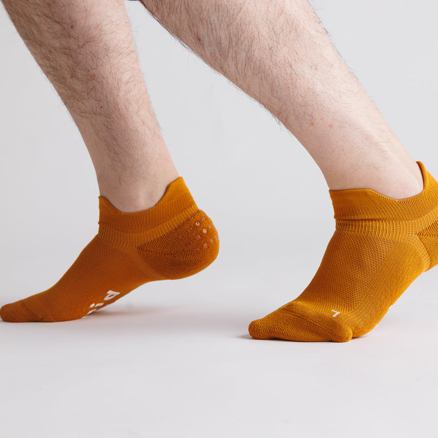 Mustard yellow ankle grip socks worn with heels raised, showing side views. By Squid Socks.
