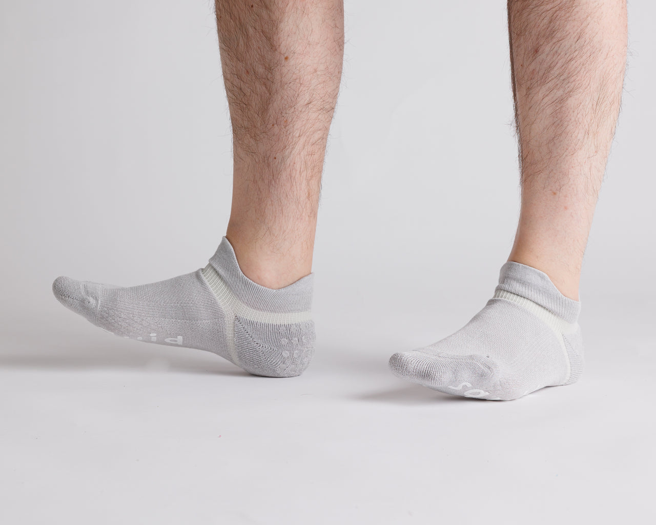 Gray ankle grip socks worn with toes raised, showing side views. By Squid Socks.