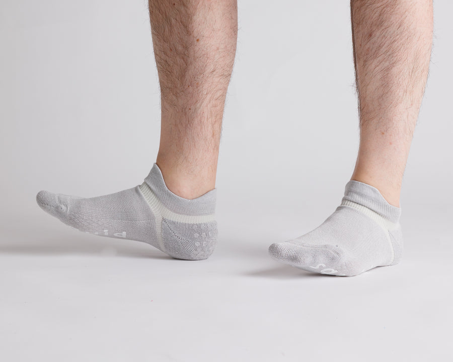 Gray ankle grip socks worn with toes raised, showing side views. By Squid Socks.