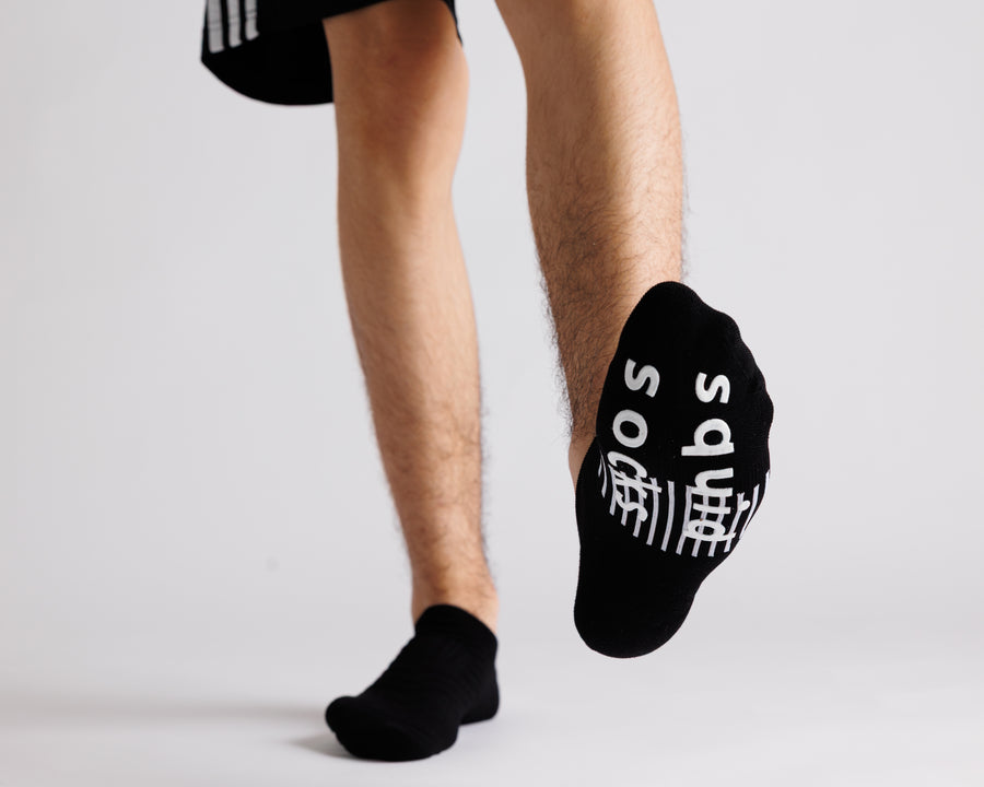 Black no-show grip socks with one foot lifted to show white bottom grips. By Squid Socks.
