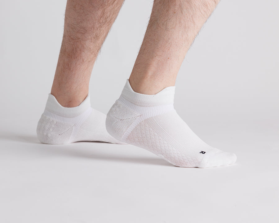 White ankle grip socks worn with heels raised, showing side views and heel tabs. By Squid Socks.