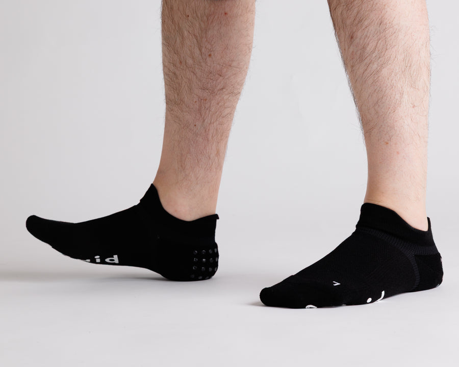 Black ankle grip socks worn with toes raised, showing side views. By Squid Socks.