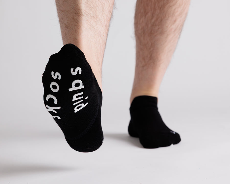 Black ankle grip socks with one foot lifted to show white bottom grips. By Squid Socks.